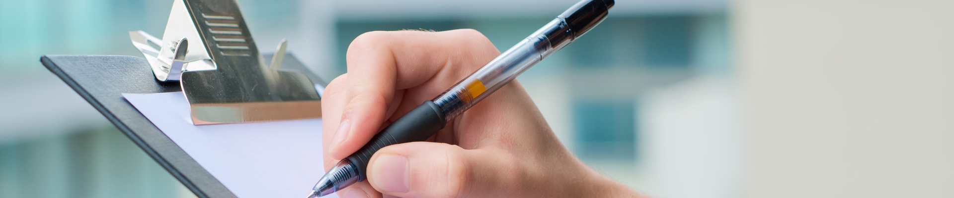 Detailaufnahme einer Person, die einen Stift in der Hand hält und damit auf ein Klemmbrett schreibt.