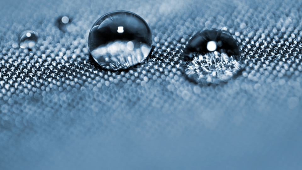 Das Bild zeigt eine Nahaufnahme von Wassertropfen auf einer schuppigen Metall-Oberfläche.