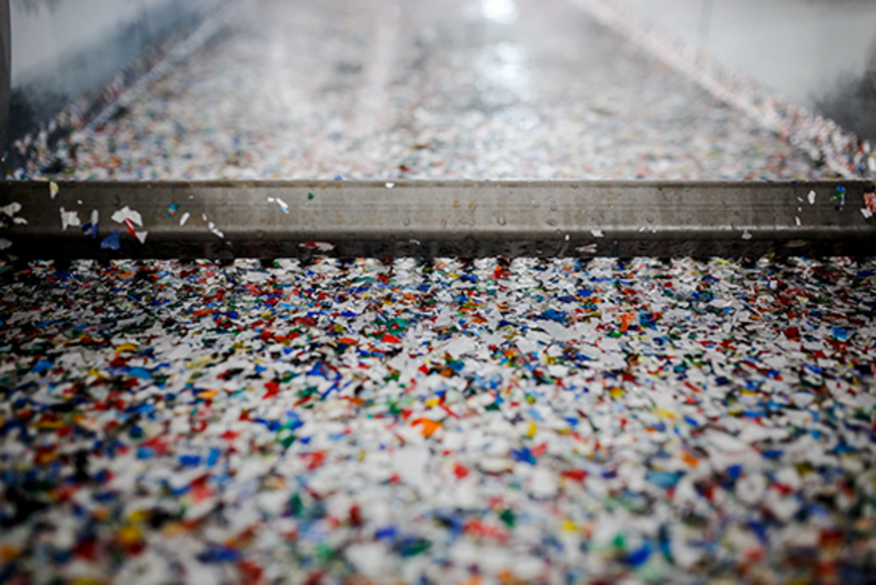 Das Bild zeigt eine Detailaufnahme von recycelten Plastikflaschen in Form von Flakes und zerkleinerte Abfälle in einer Maschine, die für das Recycling eingesetzt wird.
