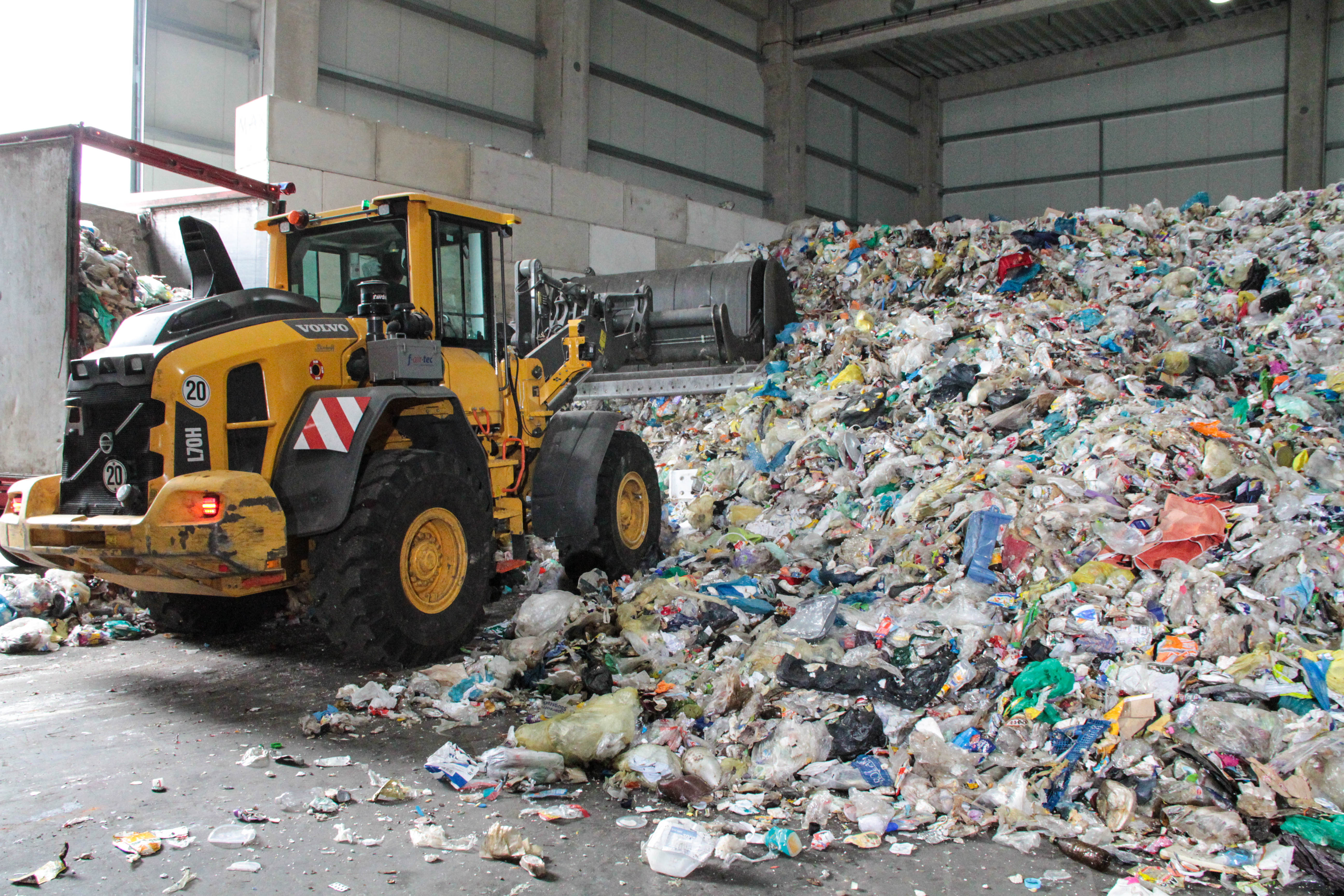 Das Bild zeigt einen Bagger, der Plastikabfall an einen Müllberg aus Plastik heranfährt.