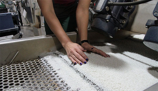 Das Bild zeigt recyclete Kunststoff-Drops in weiß in der Nahaufnahme. Eine Frau bewegt ihre Hände in den Drops.