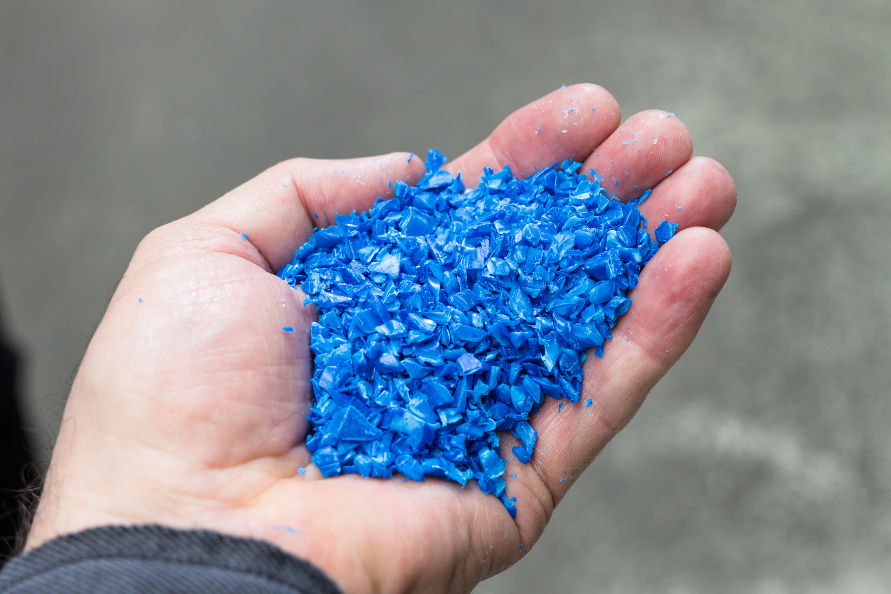 Das Bild zeigt einer Hand, die mit blauem Kunststoffgranulat gefüllt ist.