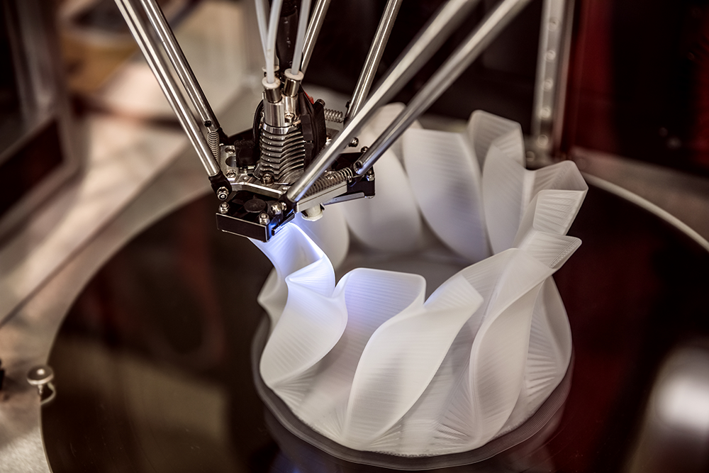Das Bild zeigt einen 3D-Drucker, der mittels additiver Fertigung unter Computersteuerung einen weißen Gegenstand aufbaut.