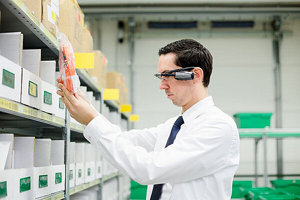 Das Foto zeigt einen Mann, der Smart Glasses trägt und damit Objekte in einem Warenlager scannt.