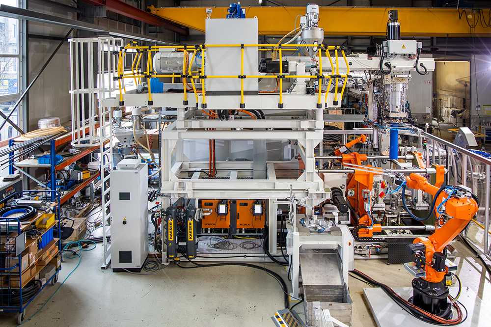 Blick in eine Fabrikhalle. Zu sehen sind Anlagen und Maschinen. Prägnant sind orange Roboterarme.