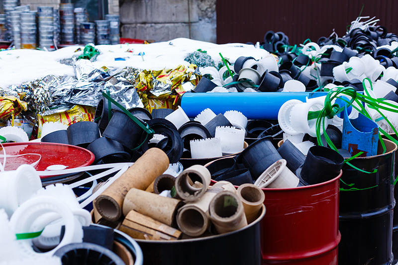 Mülltonnen auf einer Straße in der Stadt. In den Tonnen sind verschiedene Abfälle (z.B. Plastikrohre) getrennt voneinander gesammelt.