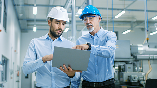 Projektleiter hält Laptop in der Hand und diskutiert Produktdetails mit Chefingenieur, während sie durch moderne Fabrik gehen.
