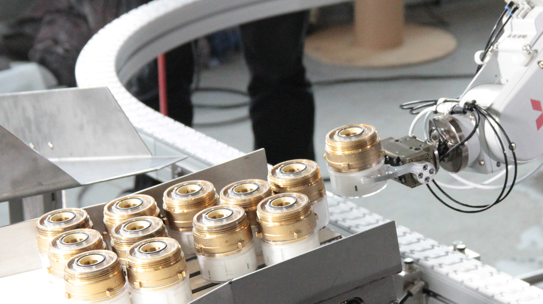 Das Foto zeigt einen Roboterarm im industriellen Umfeld, der Wasserzähler greift und von einem Punkt zum anderen transportiert. 